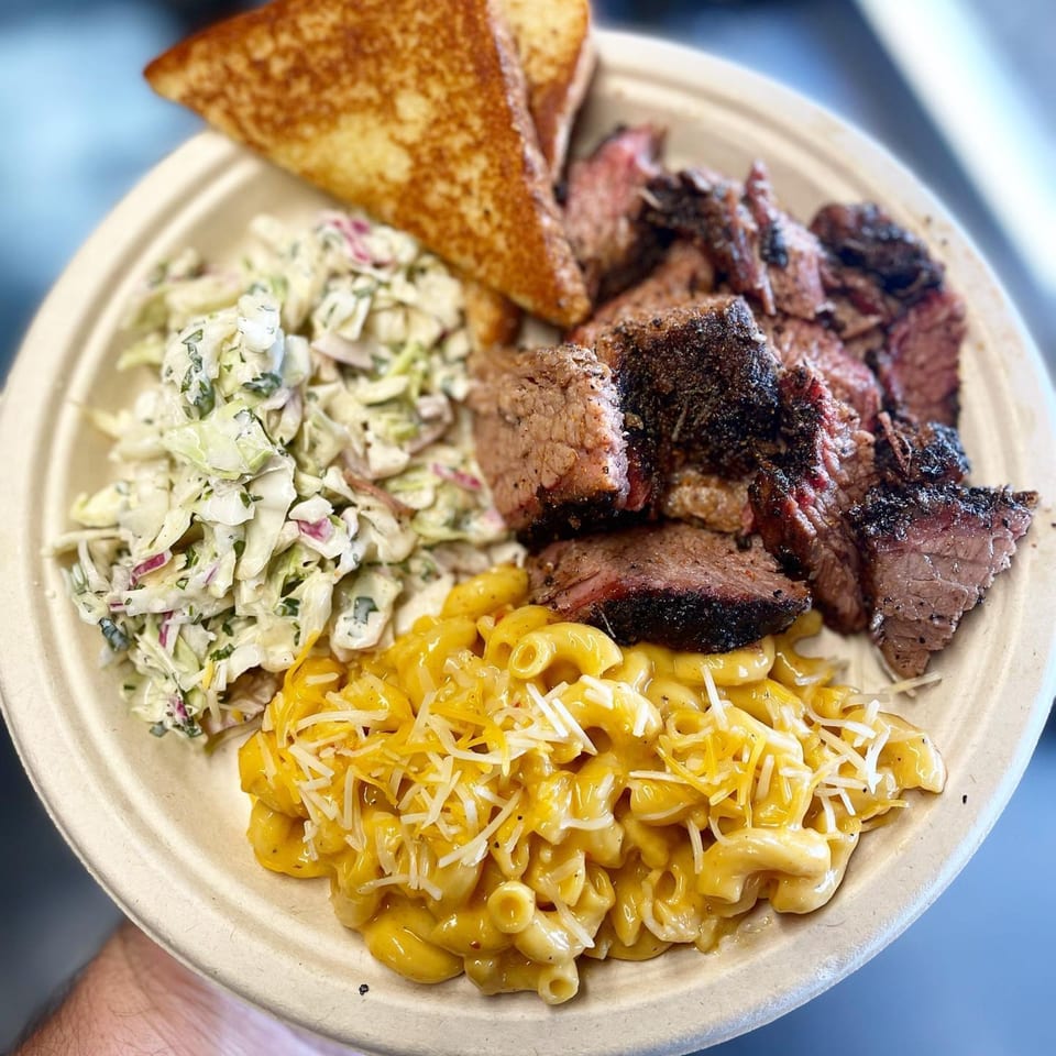 A BBQ plate with sliced brisket, creamy mac and cheese, coleslaw, and toasted bread.