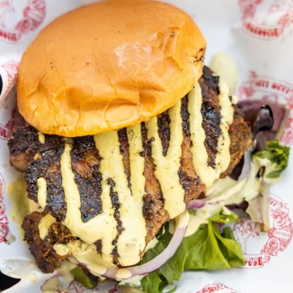 Close-up of a Butt Hutt Smokehouse BBQ sandwich with grilled meat, sauce, lettuce, and red onion.