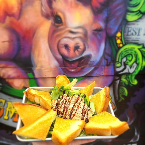 Pulled pork salad with garlic toast points and balsamic glaze, against a vibrant pig mural.