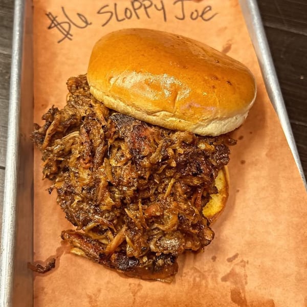 A Butt Hutt Smokehouse Sloppy Joe sandwich with pulled pork and onions on a bun.
