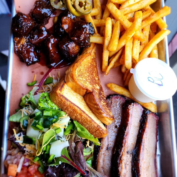 A Butt Hutt Smokehouse BBQ platter with brisket, burnt ends, fries, Texas toast, and a side salad.